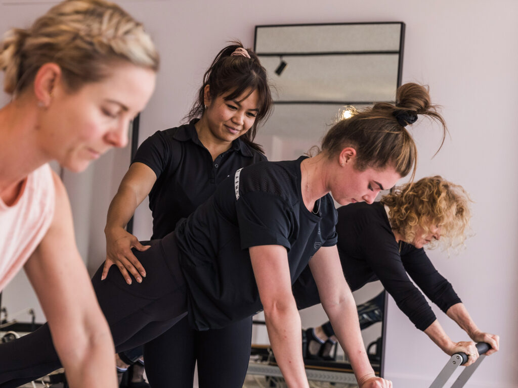 Reformer pilates instructor guiding movements on reformer carriage